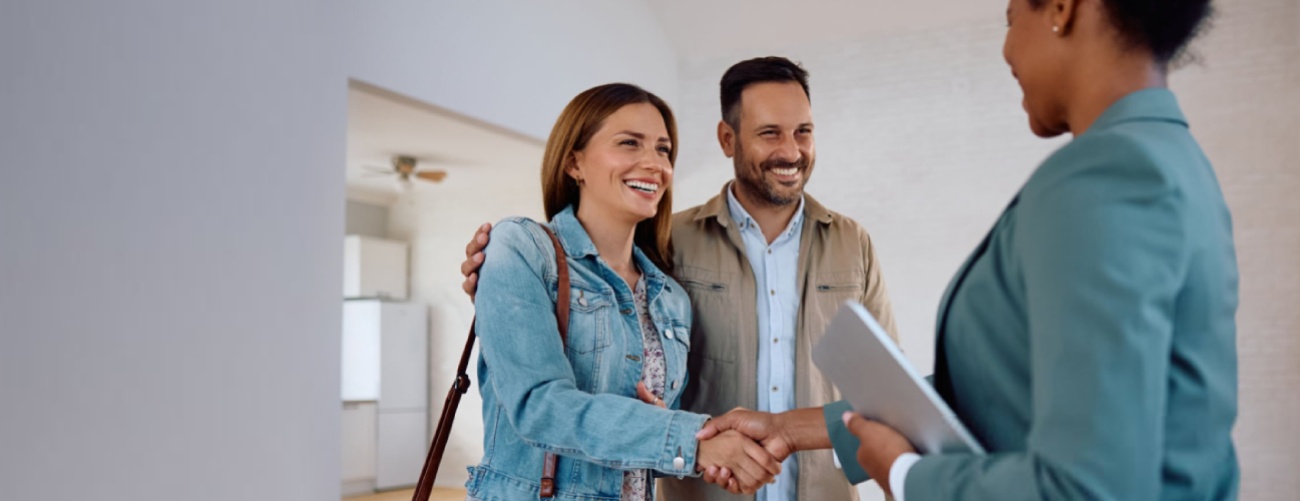 Happy woman shaking hands with real estate agent while buying new apartment with her husband, illustrating the role of real estate consultant