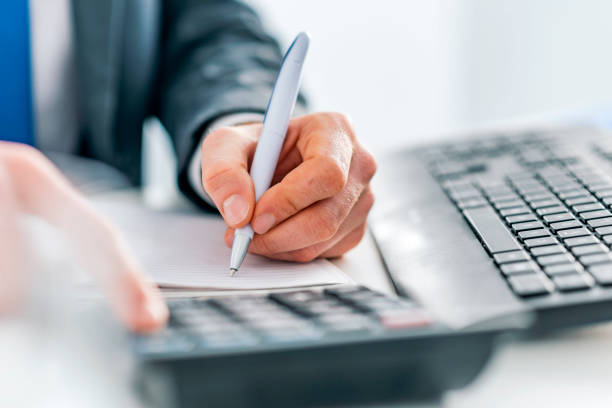 Photo of Male accountant calculations and analyzing data with calculator, Financing, Accounting, Doing finance, Economy, Savings Banking Concept. Close up, business man or lawyer accountant working on accounts using a calculator and writing on documents while sitting on his desk in modern office.