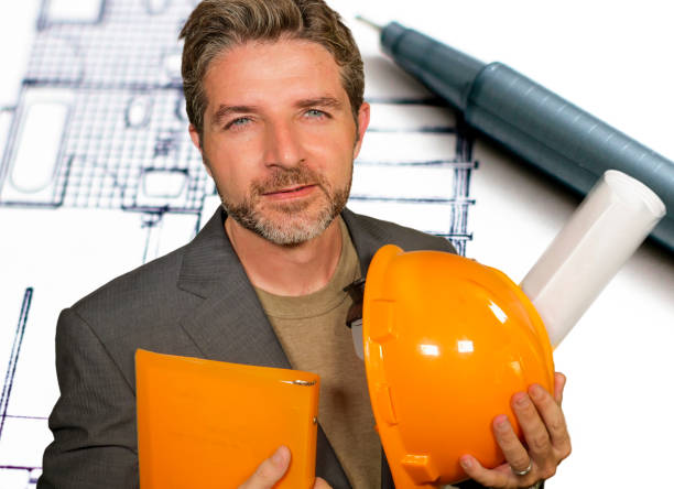 corporate portrait of attractive efficient and confident architect man holding builder helmet and building construction blueprints isolated in architecture development and business success