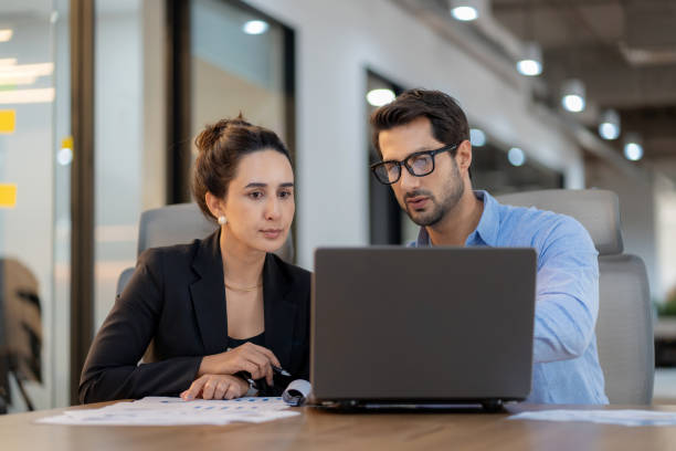 Future business planning with data-driven insights. A male project leader works with a diverse female team in a high-tech office, discussing finance, strategy, and innovation. Corporate leadership, collaboration, and digital transformation in action.