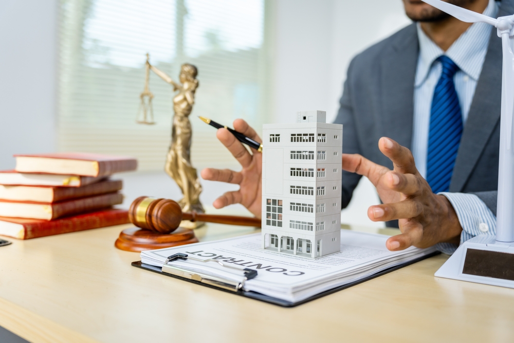 A male Asian lawyer in a formal suit works at his desk, focusing on contracts, legal matters, and urban planning issues such as building models, zoning, ordinances, and municipal regulations.