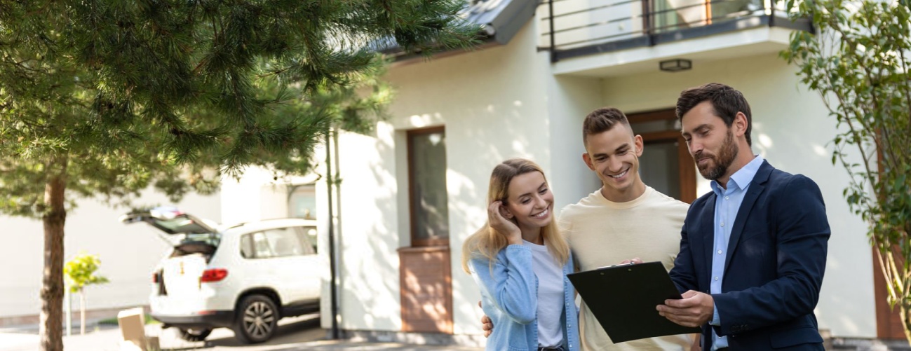 Real estate agent presenting clipboard with documents to couple in front of residential property in suburban outdoor setting