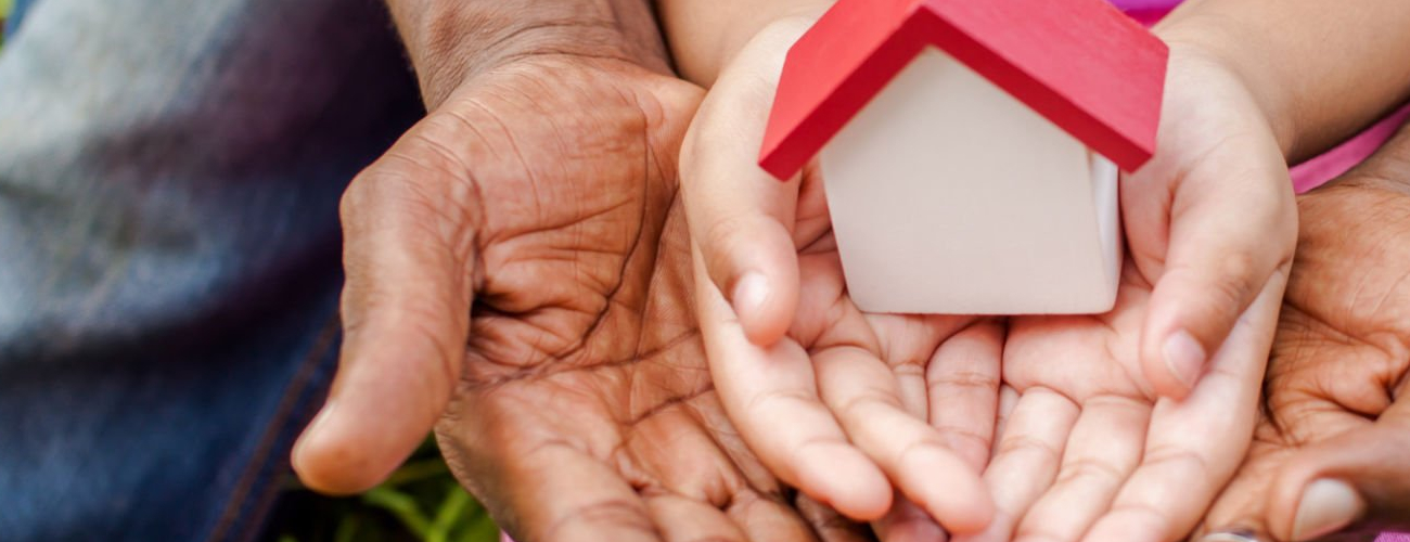 Hands of family together holding house in green park - family home and real estate concept