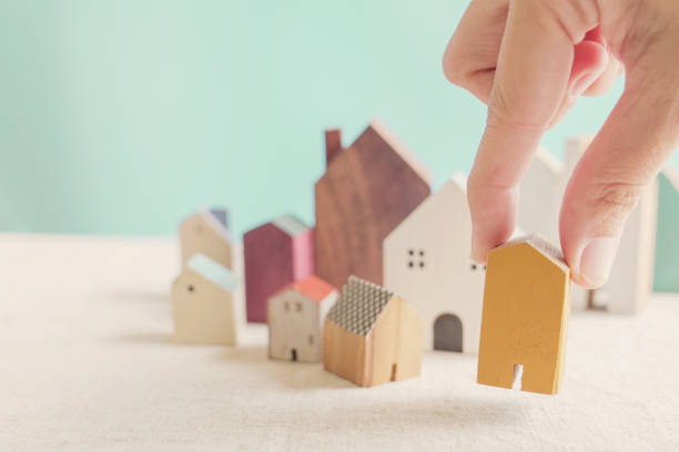 Hand choosing yellow miniature house, searching right property in high demand housing boom, making decision on home investment concept