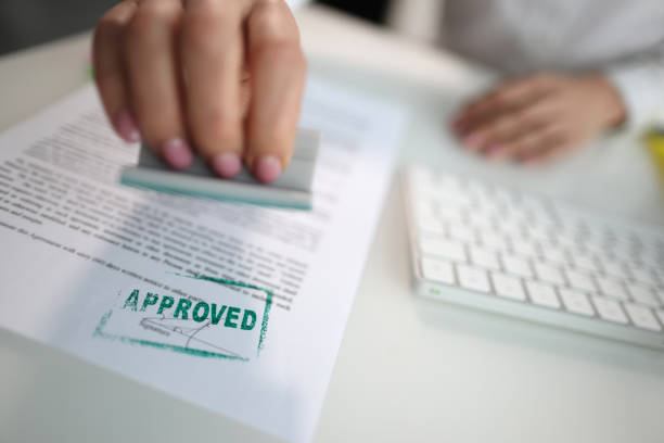Closeup of a person hand stamping green approved seal on text approved document on table. Contract form and business agreement with partner