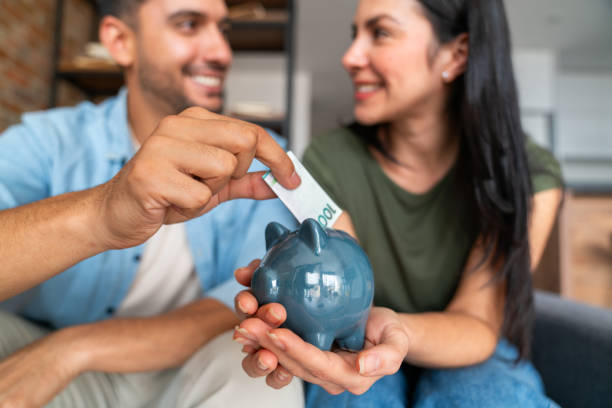Happy Latin American couple at home saving money in a piggybank and smiling