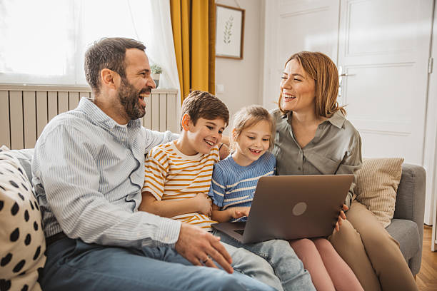 Mother and father using laptop with their children on the sofa at home. Online shopping or talking on video call.