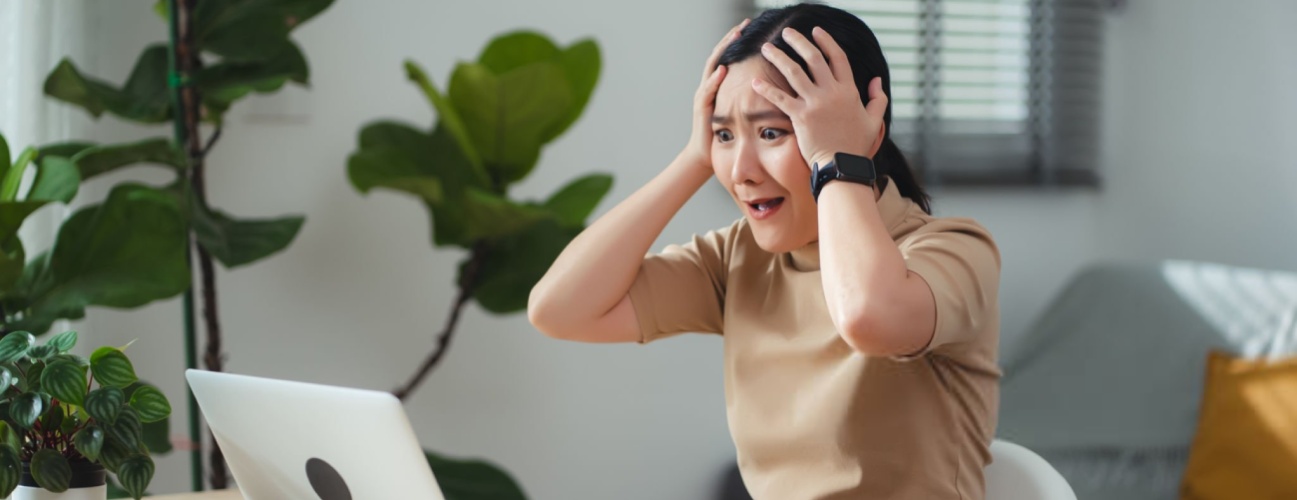 Asian woman sitting at home office thinking about problem with work, shock and feels concerned while looking at laptop.