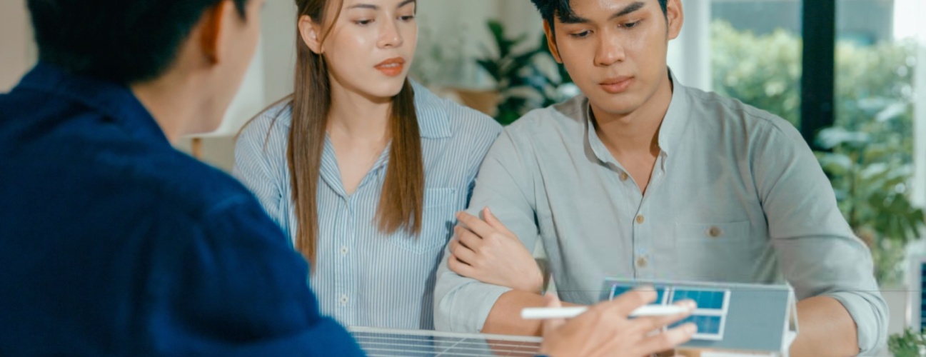 Young Asian couple in detailed consultation with real estate agent, who is highlighting advantages of home with solar panels. Consulting on Eco-Friendly Home Ownership with Real Estate Agent Concept.