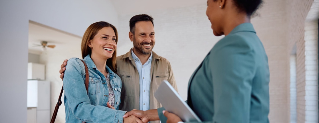 Happy woman shaking hands with real estate agent while buying new apartment with her husband.