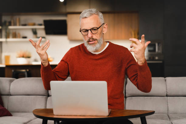 Angry troubled caucasian mature middle-aged man businessman freelancer talking with clients colleagues business partners online on laptop, solving problems, explaining at home remotely