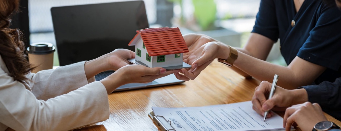 Young married couple talking to a real estate agent to sign a house purchase contract.