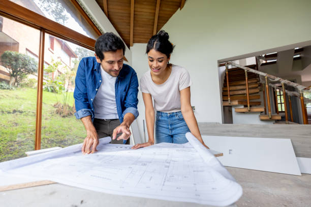 Happy Latin American couple looking at the blueprints while renovating their house