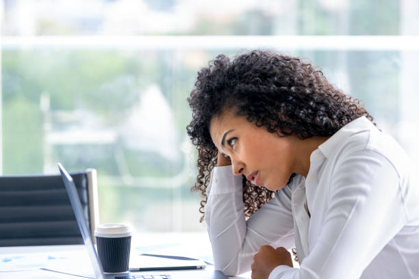 Upset woman working on a laptop computer in the office. She looks worried, frustrated and depressed. She has her head in her hands