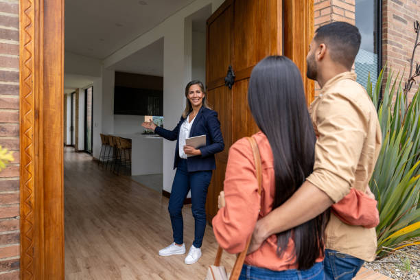 Happy real estate agent welcoming a Latin American couple for a showing at a house for sale