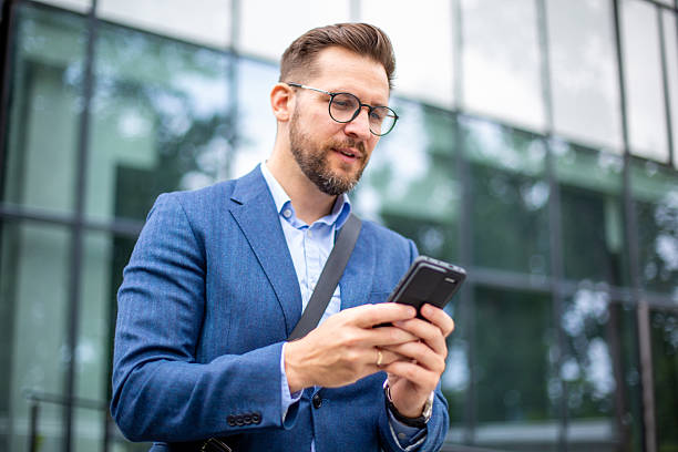 Businessman texting on his smartphone in front of a modern office building