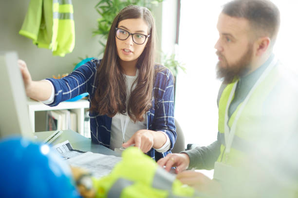 a female construction engineer apprentice chats to her colleague over some building plans