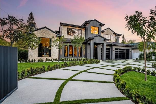 Modern luxury home exterior with a well-manicured lawn, geometric driveway, and sunset sky in the background.