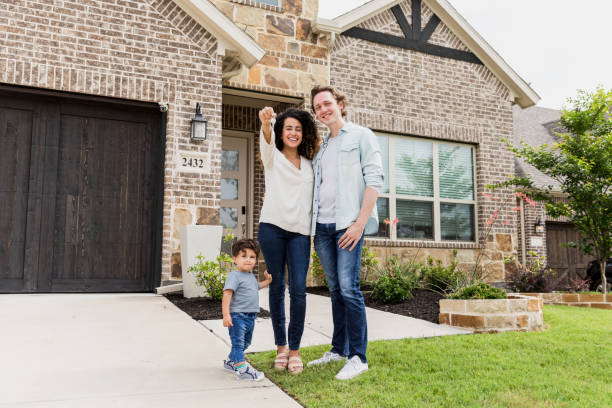 Young family stands proudly in front of their new house, holding keys.