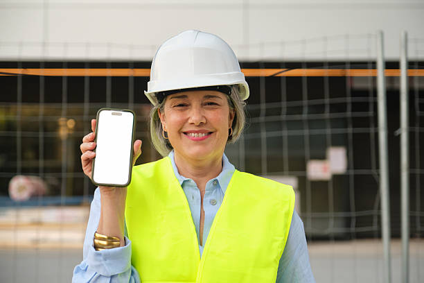 Portrait of a mature woman architect or engineer smiling and showing smartphone with blank white screen