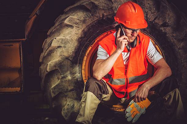 Hard Construction Business Concept with Caucasian Businessman Making Business Call While Seating Inside Heavy Duty Bulldozer Tire.