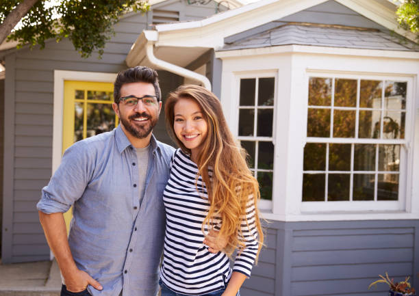 Portrait Of Excited Couple Standing Outside New Home