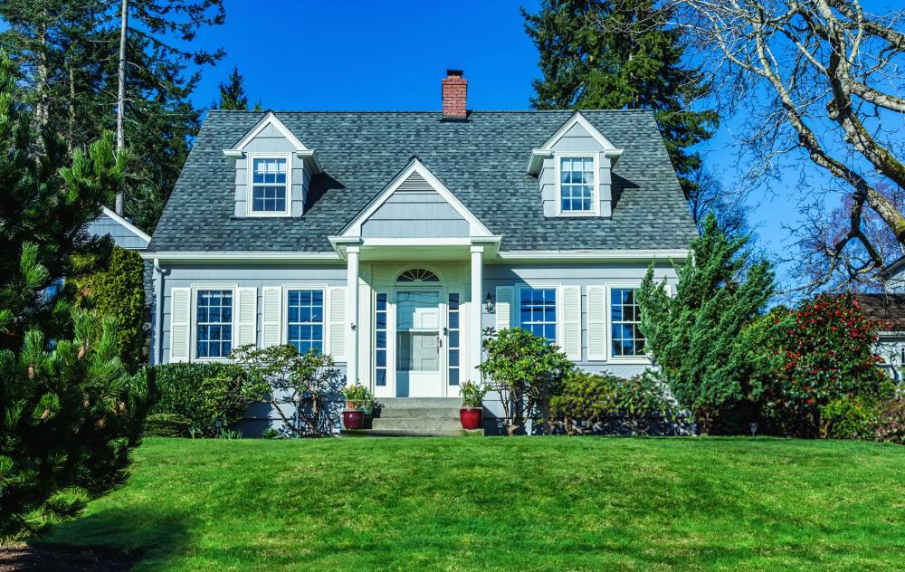 Photo of a quaint American Cape Cod Style home on a sunny day with clear blue sky and green grass.