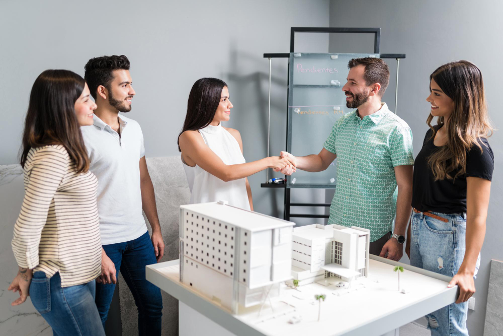 Business partners shaking hands with engineer by architectural model in meeting 