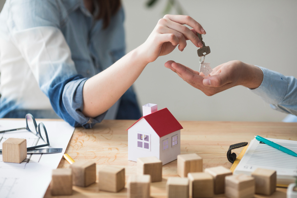 Close-up of woman's hand giving house key to man over wooden table 