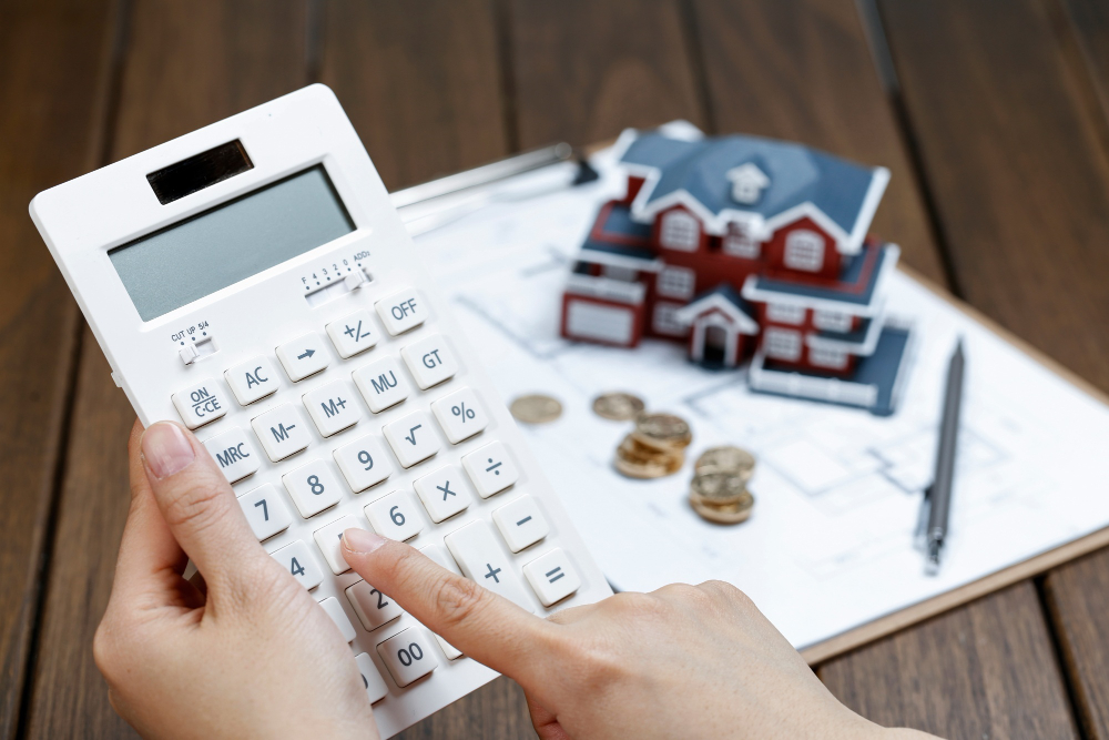 A female hand operating a calculator in front of a villa house model 