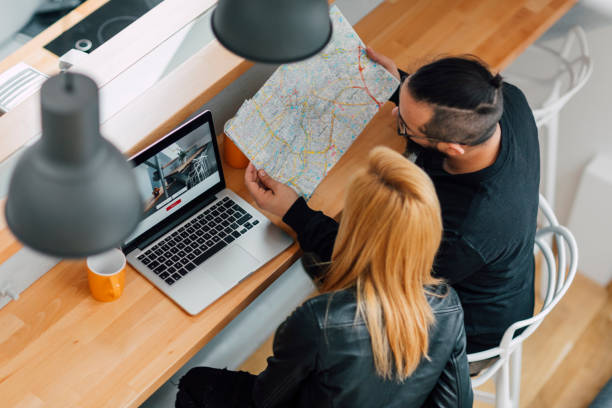 Young Hipster Couple, backpackers, looking on their laptop to rent apartment using vacation home rental services online. Looking at map and laptop. They are cheerful together. Top view