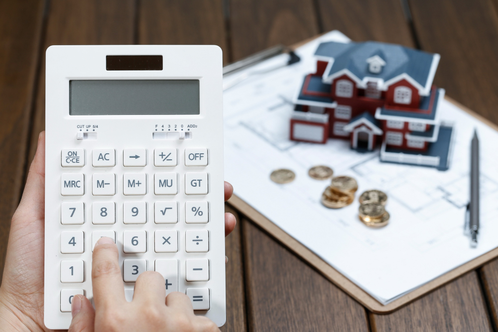 A female hand operating a calculator in front of a villa house model 