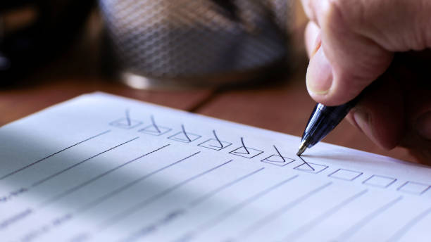 Close up image of a person’s hand using a ballpoint pen to put a check or tick mark in a row of boxes on a paper form sheet.