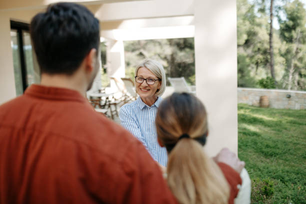 Mature female real estate agent shaking hands with young couple in front of house that they rented for vacation