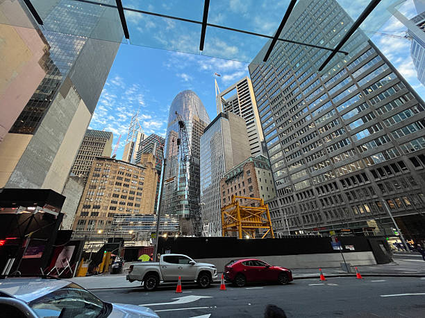 An expansive view captures an inner city construction site enclosed by looming modern skyscrapers, highlighting the contrast between ongoing development and established urban architecture