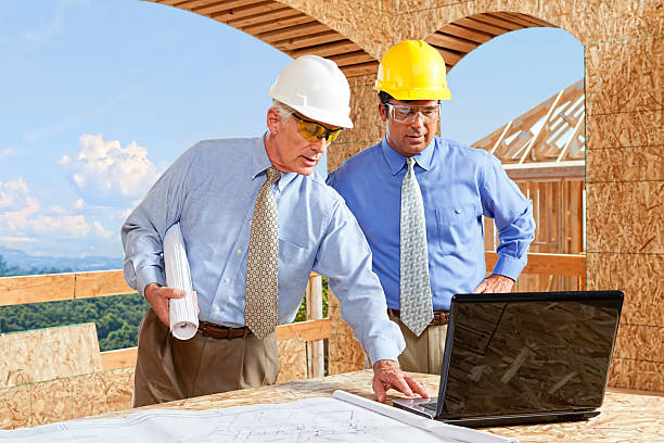 A general contractor looks over the plans and budget with the architect on a job site for a large estate home.
