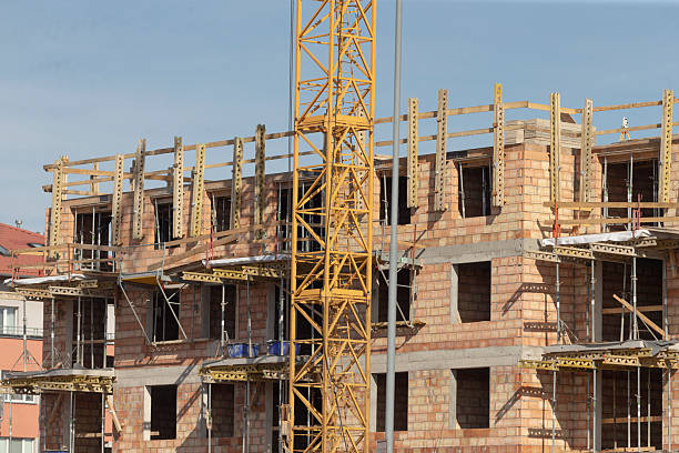 construction crane with apartment backdrop, heavy construction equipment overseeing ongoing brick apartment development, skyline view featuring tower crane amidst active building work on residential