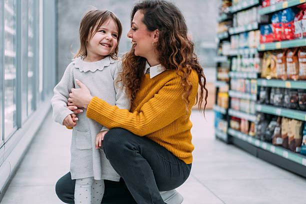 Shot of a cheerful mother and her little girl select products in a supermarket aisle. Young mom shopping with her small daughter in the grocery store.