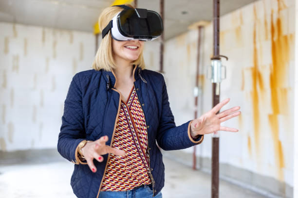 Woman wearing VR goggles standing at a construction site of her new house. Female owner using augmented reality glasses on building site.