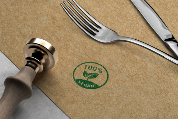 A close-up shot of a 100% vegan stamp on an eco-friendly brown napkin, placed alongside a polished silver fork and knife with a modern handle, symbolizing sustainable and ethical dining choices.