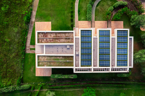 Aerial view of a modern eco-friendly building featuring solar panels and green roofs, surrounded by lush landscaping and sustainable architecture.