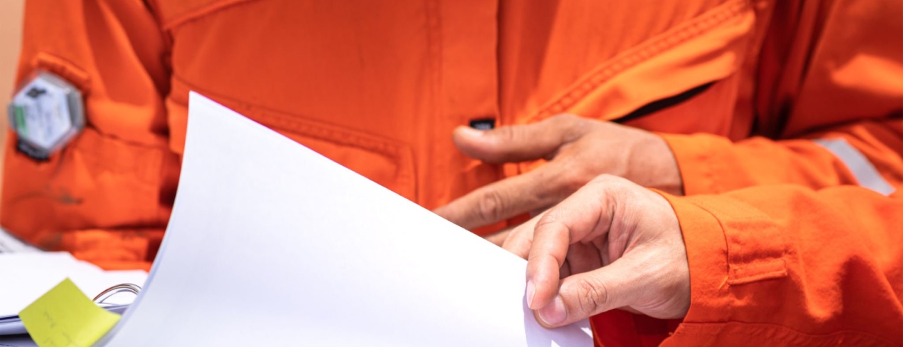 A worker in orange coverall uniform is opening documents to make a discussion on working procedure, safety audit in operation action photo. Close-up and partial focus on human's hand part.
